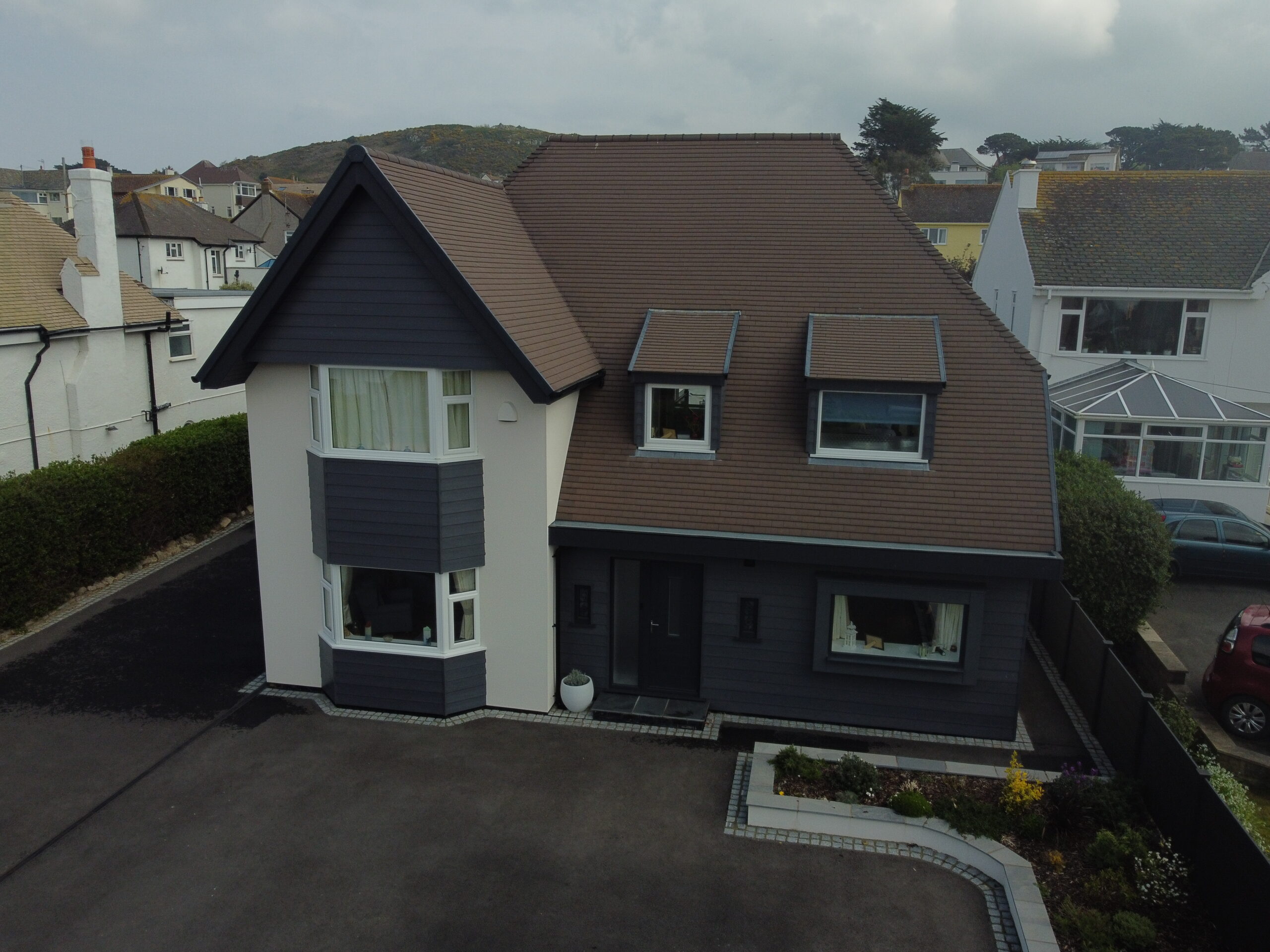 An aerial shot of a recently refurbished black and white house with brown roof.