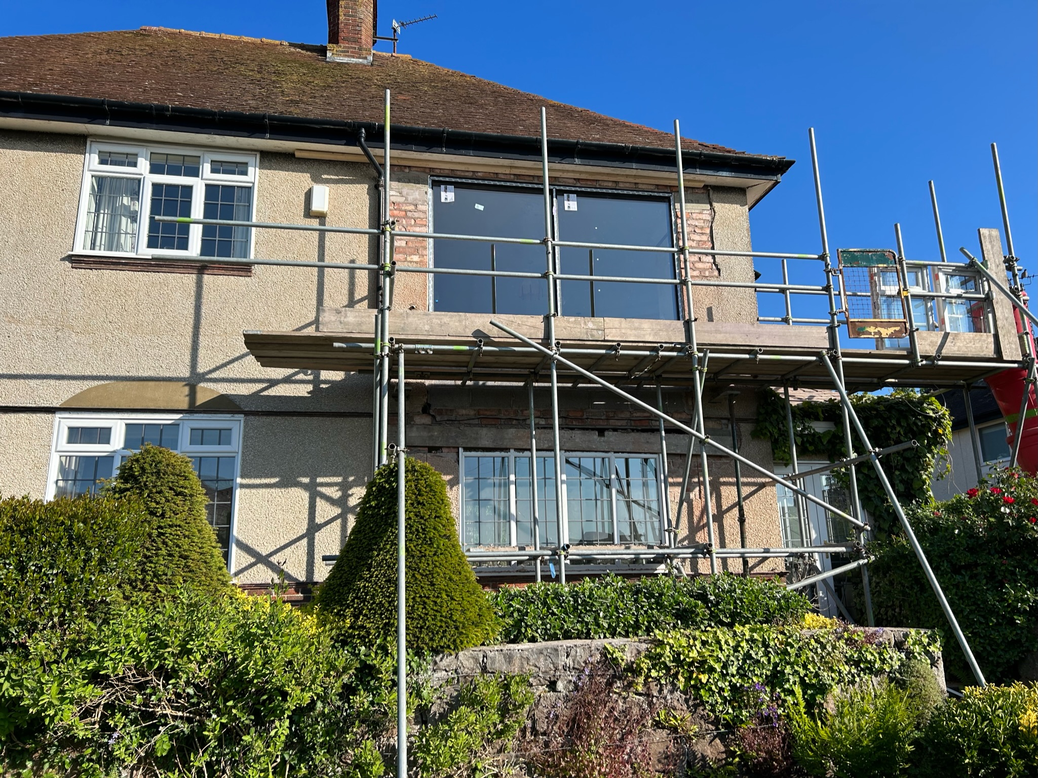 Scaffolding on the back of a house with a new large window on the second floor.